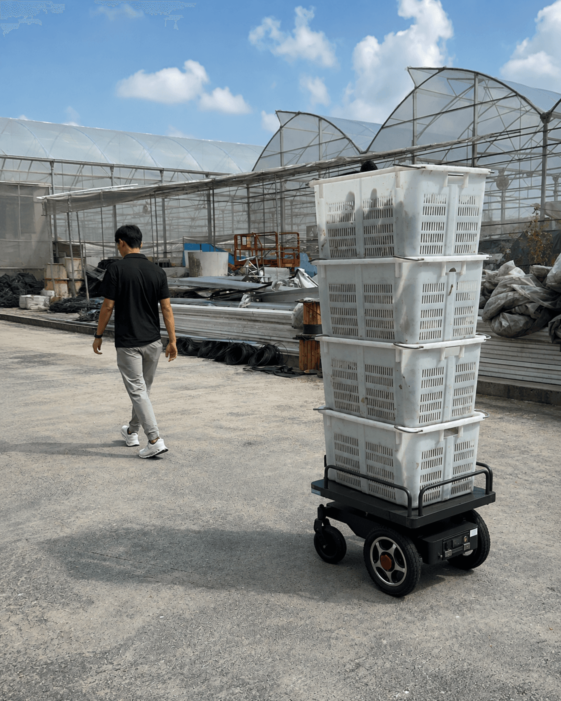 AMT100 carrying stacked produce crates across an outdoor farm yard, following a worker